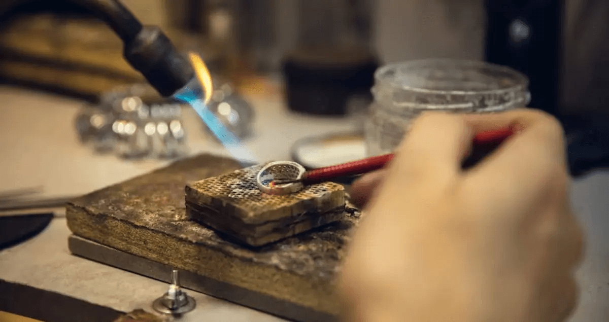 A jeweller soldering a ring at the workbench with a torch