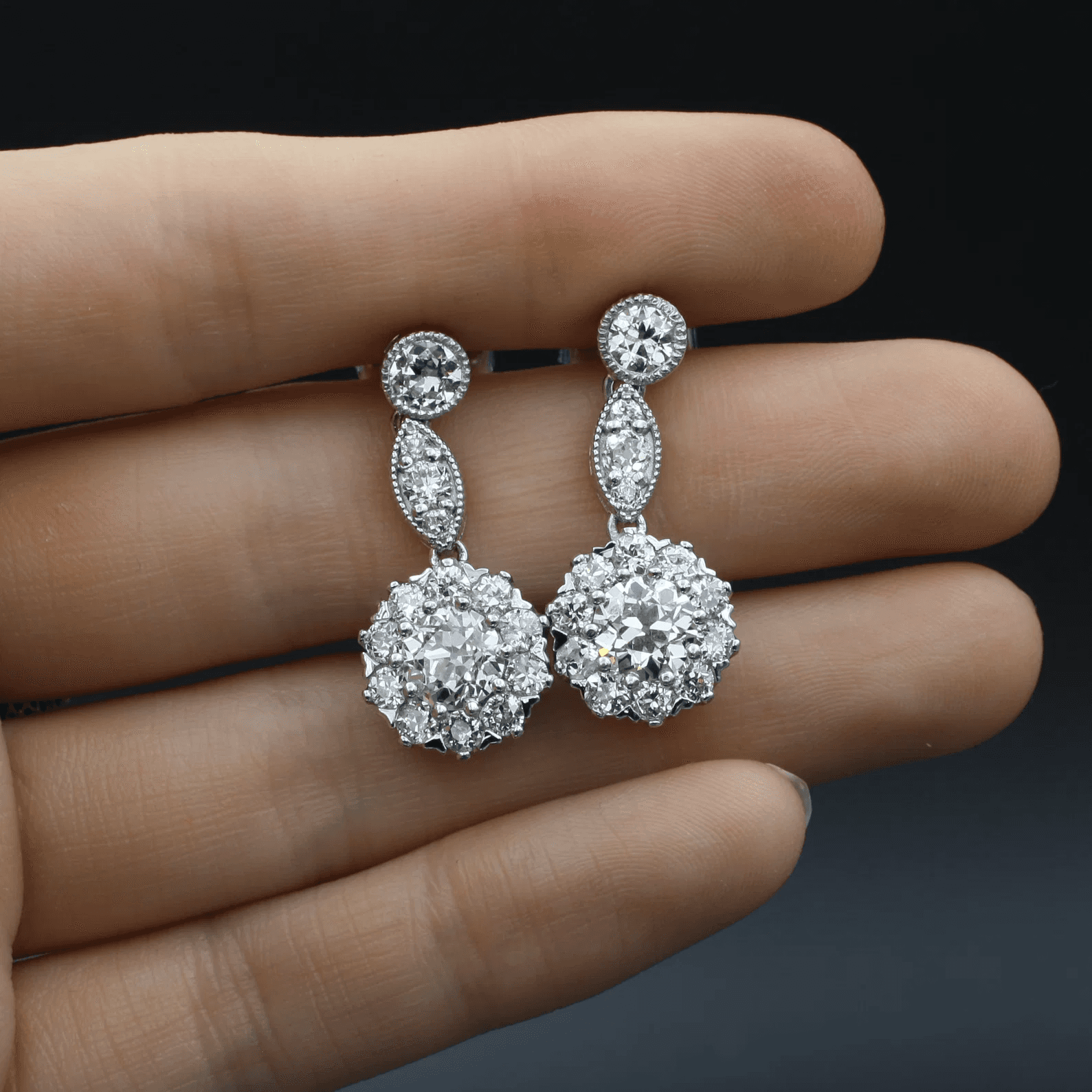 A pair of diamond cluster drop earrings held between two fingers